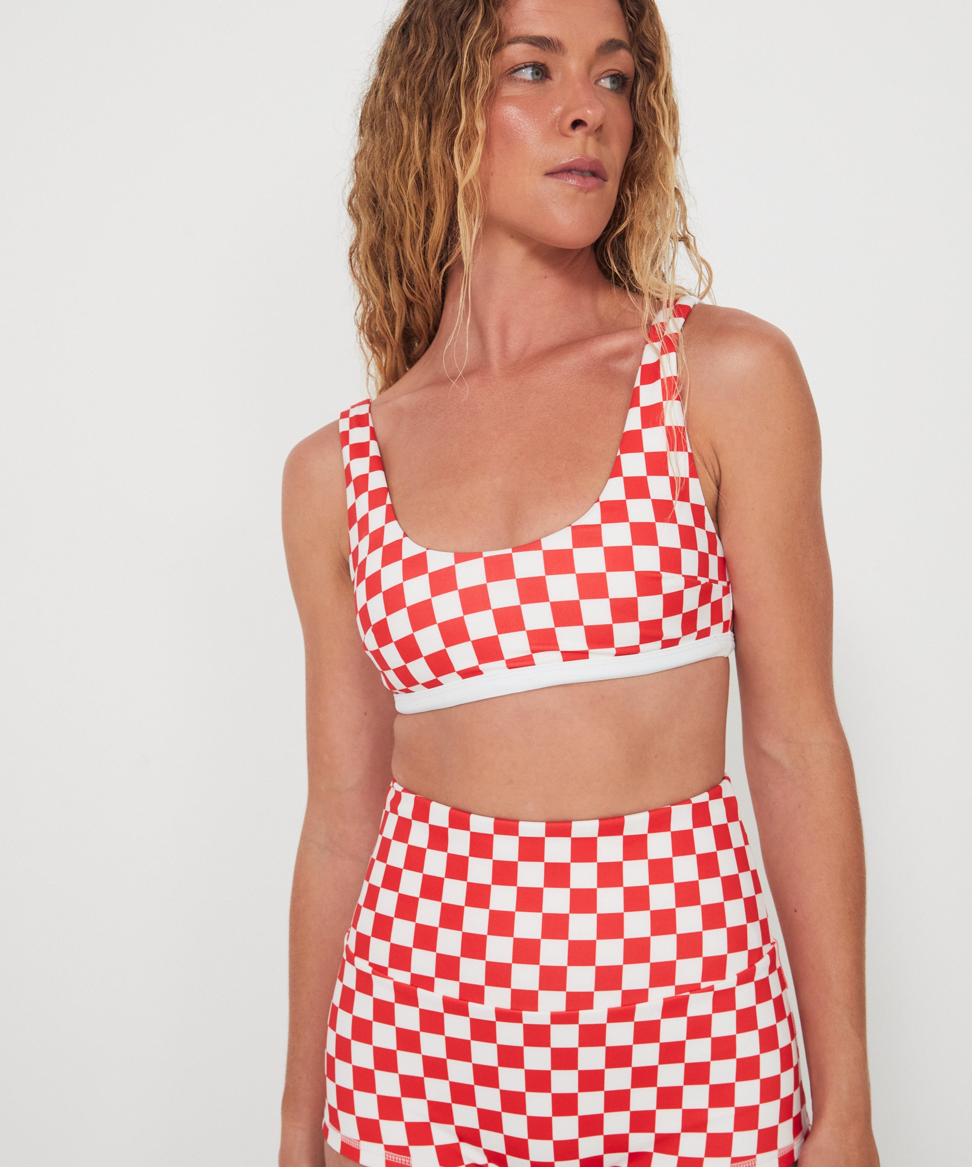 Woman wearing a red and white checkered two-piece, bralette swim top and original betty bottoms outfit on a plain background