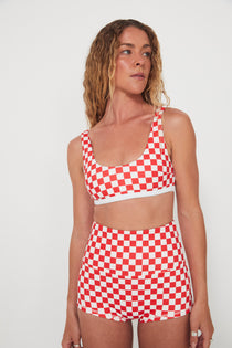 Woman wearing a red and white checkered two-piece, bralette swim top and original betty bottoms outfit on a plain background