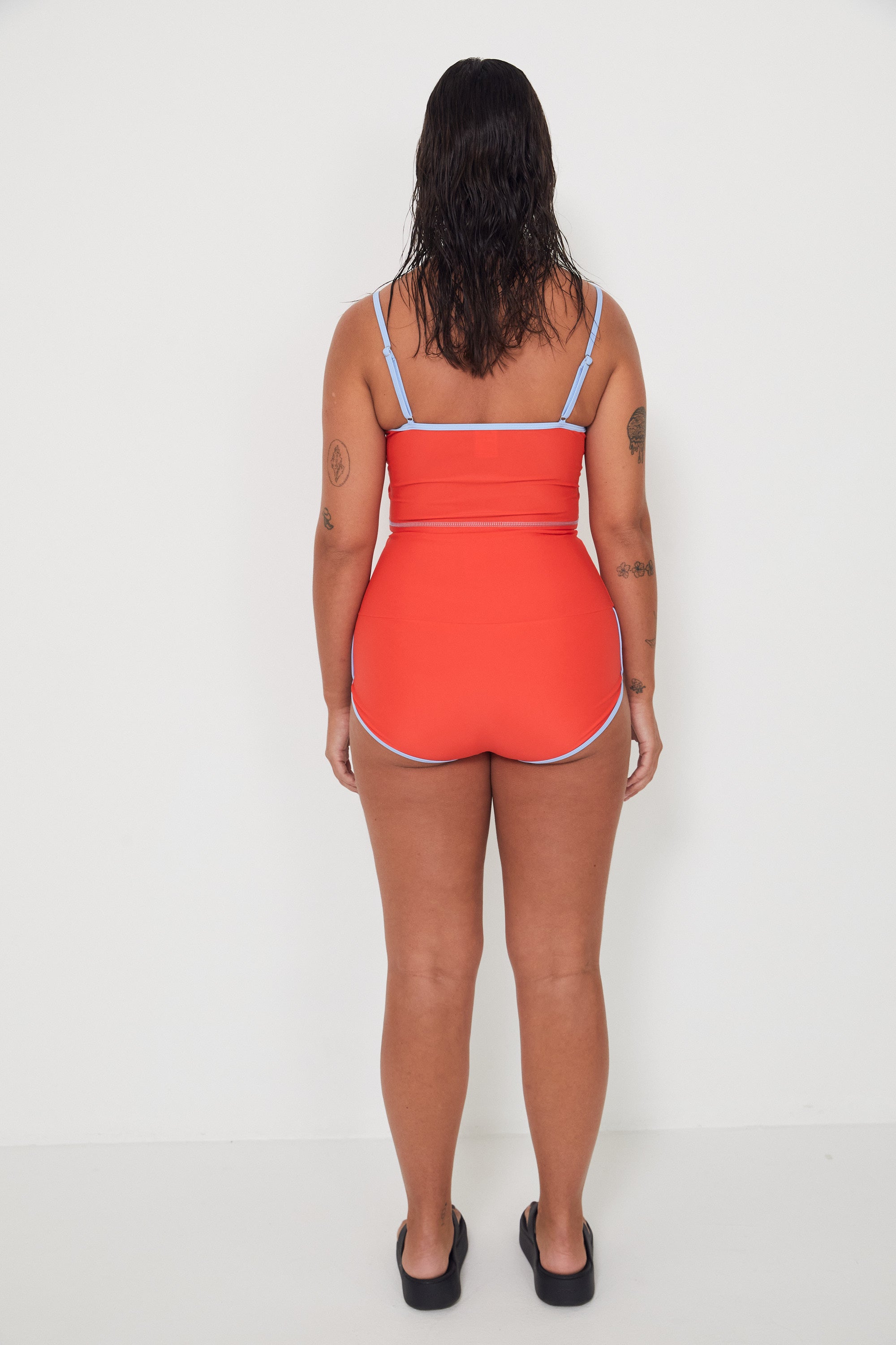 Woman wearing a red tankini surf top and betty bottoms 2.0 with blue trim on a white background