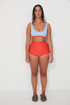Woman wearing a light blue sports and swim bra and red swim shorts on a white background