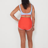 Person wearing a light blue sports and swim bralette and bright red swim shorts on a white background