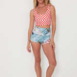 Woman wearing a red and white checkered punchy surf top and patterned original betty bottoms shorts on a white background