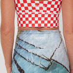 Person wearing a red and white checkered punchy surf crop top and blue shorts with graphic design.