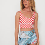 Woman wearing a red and white checkered punchy surf top and patterned ocean photographed shorts on a white background
