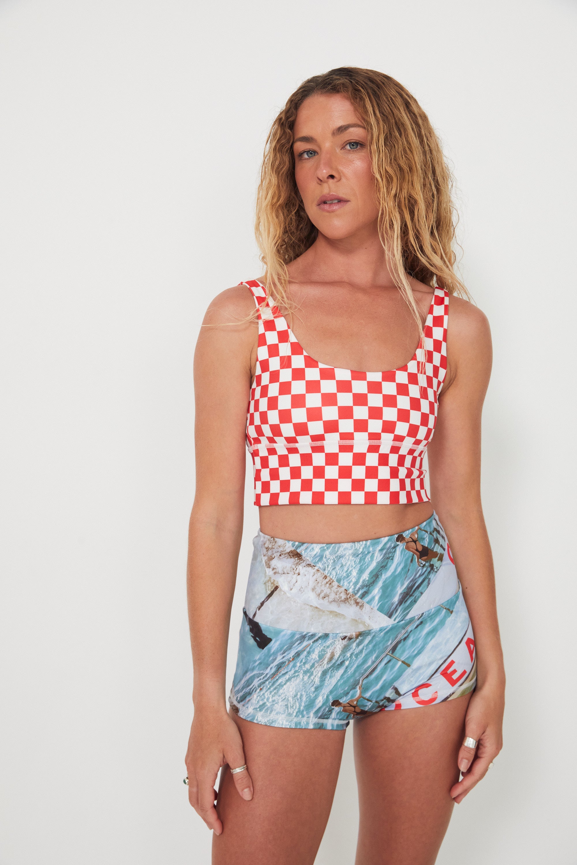 Woman wearing a red and white checkered punchy surf top and patterned ocean photographed shorts on a white background