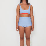 Woman wearing a light blue bralette bikini and original betty bottoms with a white background