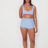 Woman wearing a light blue bralette surf top and high-waisted original betty bottom shorts on a white background