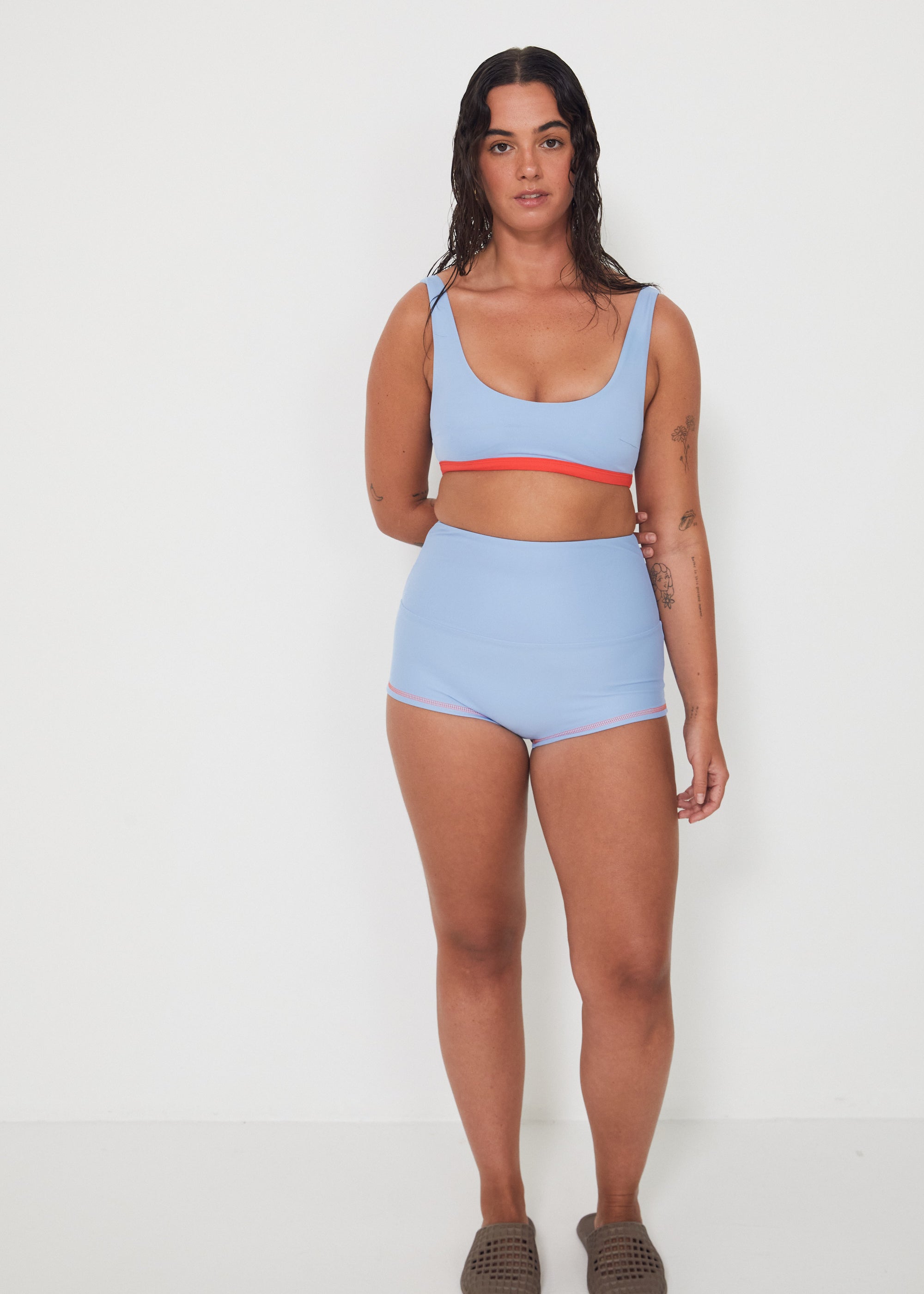 Woman wearing a light blue bralette surf top and high-waisted original betty bottom shorts on a white background