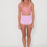 Woman wearing a red and white checkered punchy surf crop top and pink high-waisted betty bottoms 2.0 shorts on a white background
