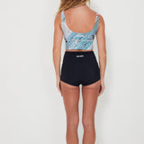 Woman wearing a patterned crop top and black shorts on a white background