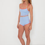 Woman wearing a baby blue tankini surf top and betty bottoms 2.0 with red trim on a white background