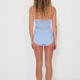 Woman wearing a baby blue tankini surf top and betty bottoms 2.0 with red trim on a white background