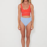 Woman wearing a red punchy bikini top and light blue high-waisted drifter bottoms on a white background