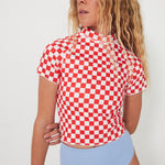 Woman wearing a red and white checkered rashguard and light blue high-waisted bottoms on a plain background