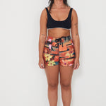 Woman wearing a black bralette swimwear crop top and vacay floral holiday swimwear boardshorts on a white background collaboration of salt gypsy and friday 