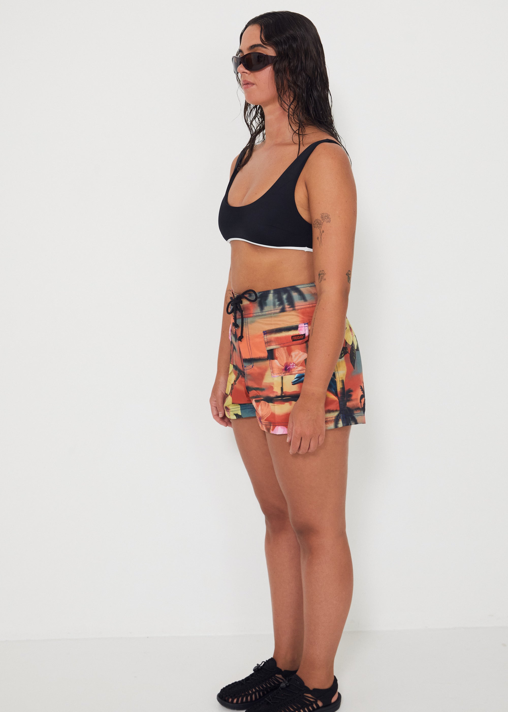 Woman wearing a black and white bralette by salt gypsy and boardsports with a vacay colorful patterned by salt gypsy and friday on a white background