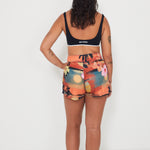 Woman wearing a black and white bralette sports swimwear bra and colorful floral and vacay print boardshorts by salt gypsy and friday on a white background