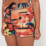 Woman wearing a colorful floral and vacay print boardshorts by salt gypsy and friday on a white background