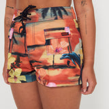 Woman wearing a colorful floral and vacay print boardshorts by salt gypsy and friday on a white background