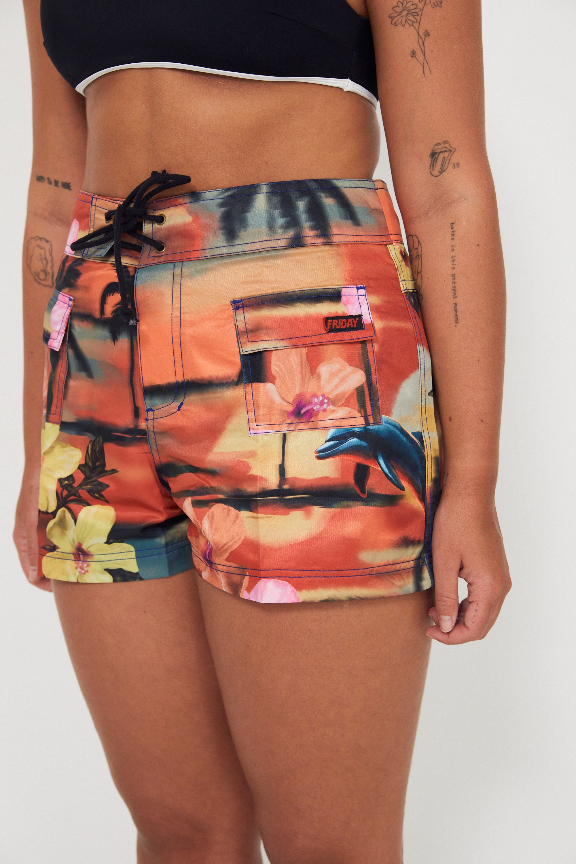 Woman wearing a colorful floral and vacay print boardshorts by salt gypsy and friday on a white background