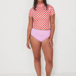 Person wearing a red and white checkered rashguard and pink high-waisted bikini bottoms on a white background