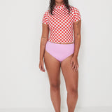 Person wearing a red and white checkered rashguard and pink high-waisted bikini bottoms on a white background