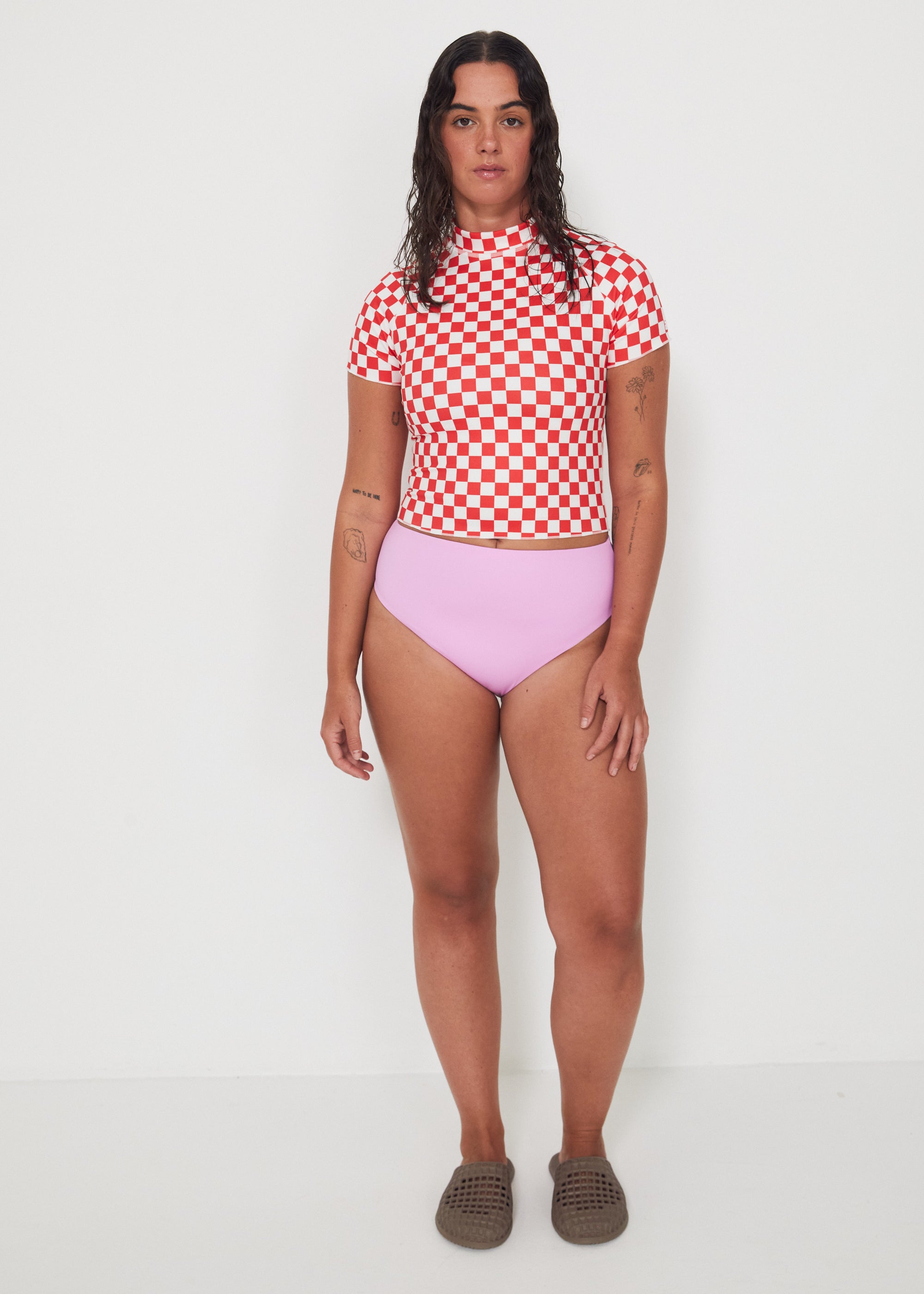 Person wearing a red and white checkered rashguard and pink high-waisted bikini bottoms on a white background