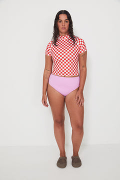 Person wearing a red and white checkered rashguard and pink high-waisted bikini bottoms on a white background