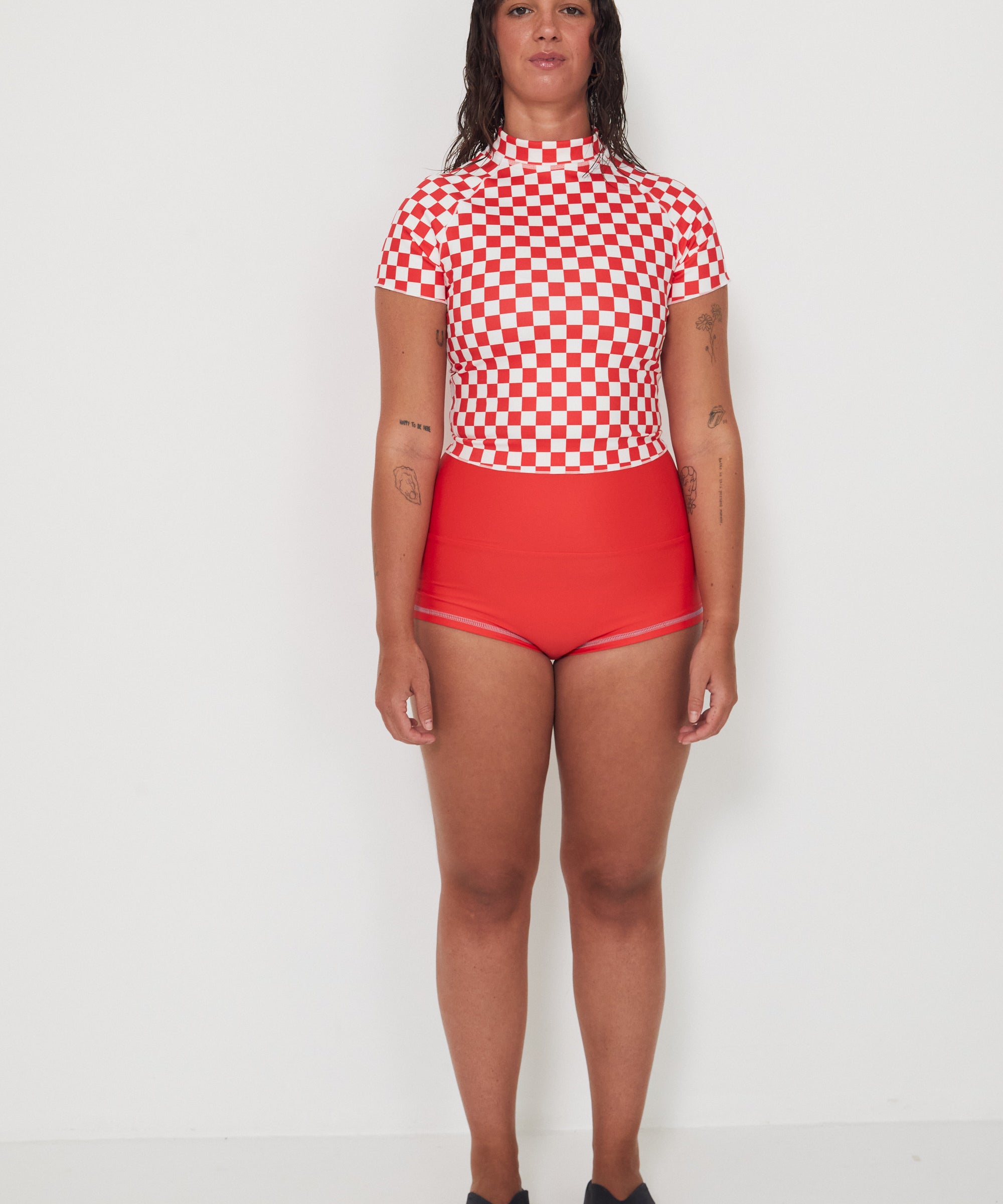Person wearing a red and white checkered low rider rashugard top and red original betty bottoms shorts on a white background
