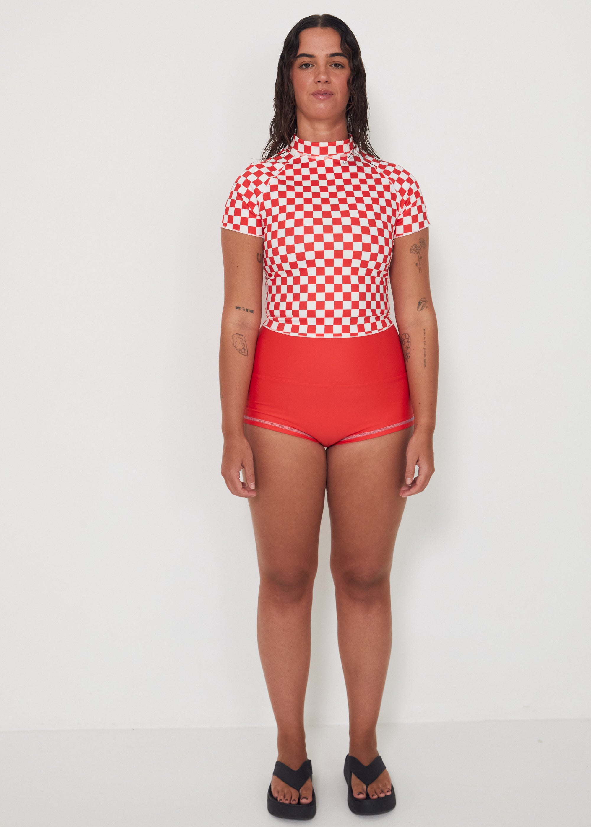 Person wearing a red and white checkered low rider rashugard top and red original betty bottoms shorts on a white background