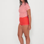 Woman wearing a red and white checkered rashguard and red shorts on a white background