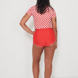 Person wearing a red and white checkered low rider rashguard and matching red original betty bottom shorts on a white background