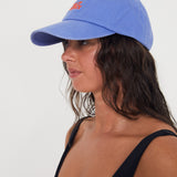 Woman wearing a blue dad cap with red writing on a white background