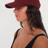 Woman wearing a maroon baseball dad cap on a white background