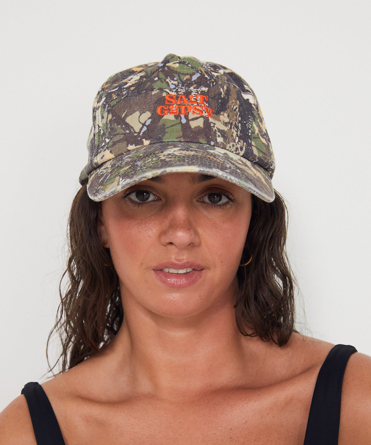 Woman wearing a camouflage dad cap with a red 'Salt Gypsy' logo on a white background