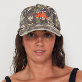 Woman wearing a camouflage dad cap with a red 'Salt Gypsy' logo on a white background